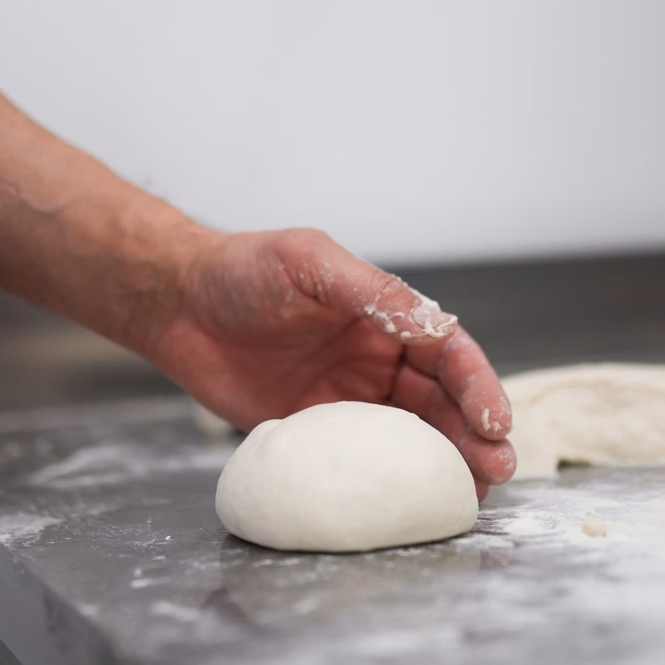 Hand formt einen Teigballen auf der bemehlten Arbeitsplatte