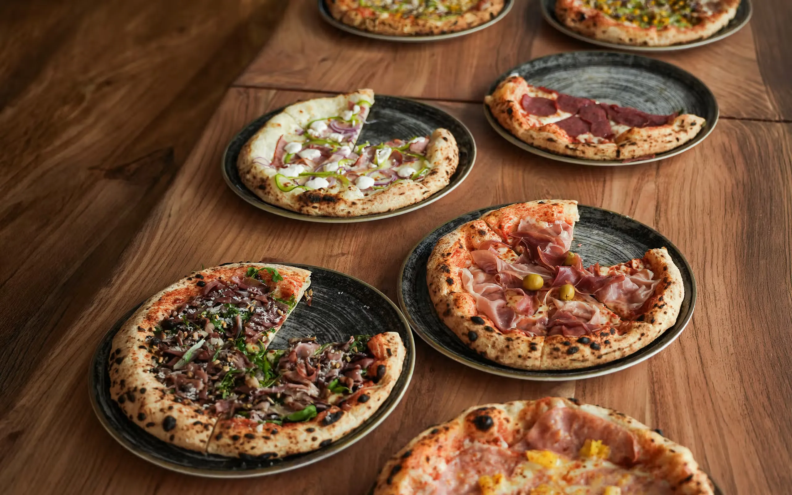 Frisch gebackene Pizzen auf einem Holztisch bei Pizza na i
